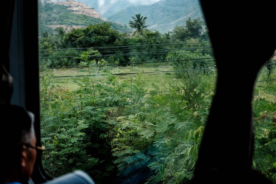 Durch das Busfenster sind grüne Felder und Berge sichtbar.