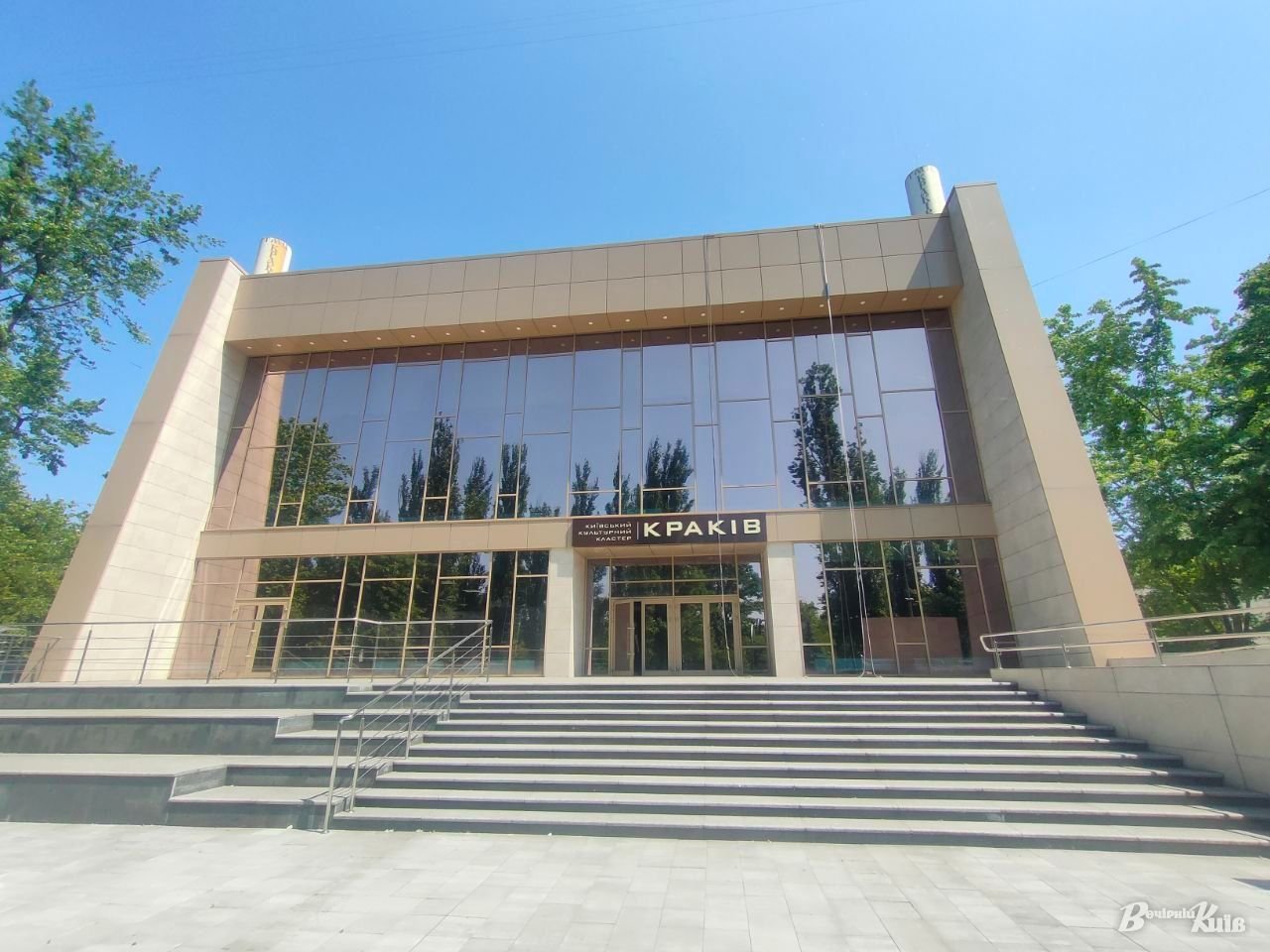 Сучасна будівля з великими скляними вікнами та сходами перед входом.