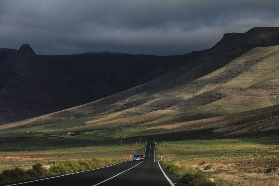 Una strada si estende attraverso colline verdi sotto un cielo scuro.