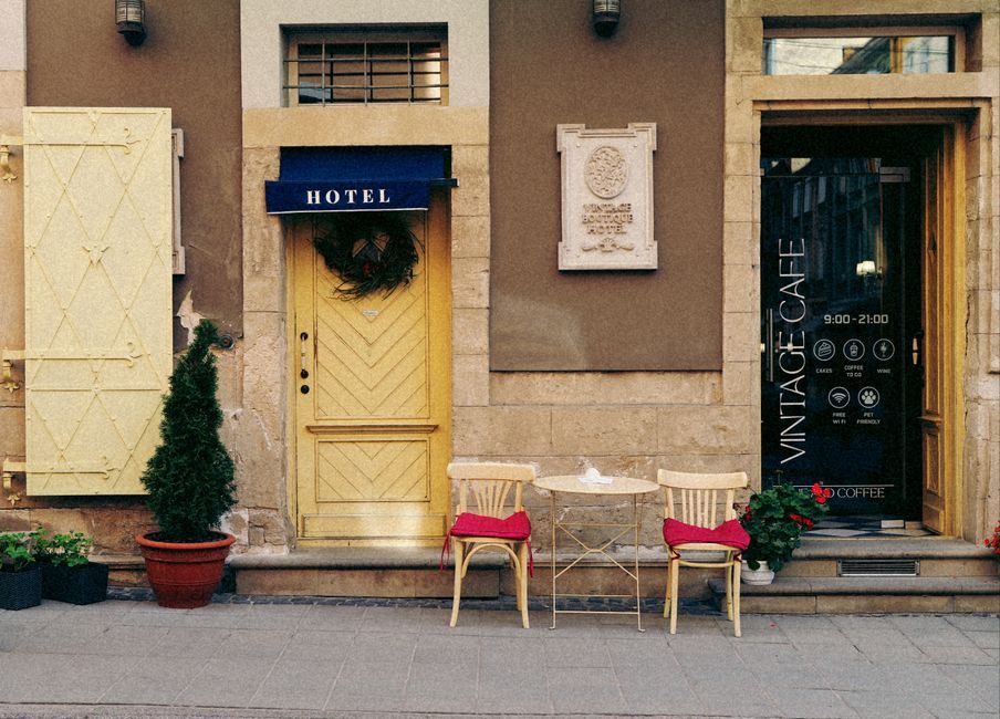 La calle muestra la fachada de un hotel con puertas amarillas y una mesa con dos sillas.