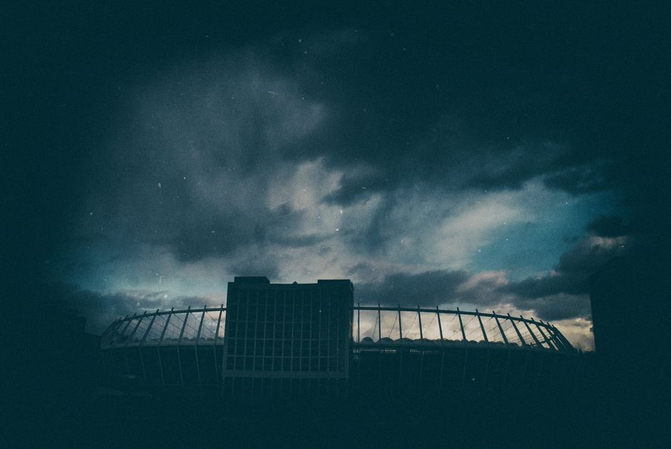 На фоні темного неба видно стадіон з арковою конструкцією.