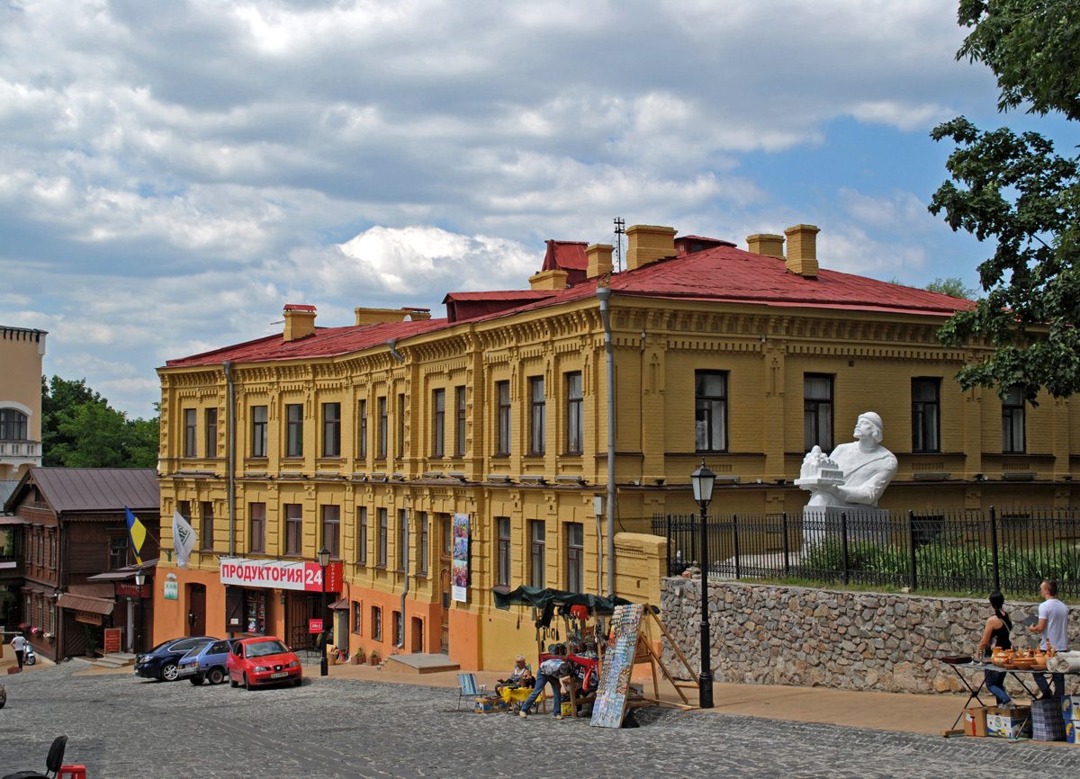На фотографії видно жовту будівлю з червоним дахом та статую на схилі.