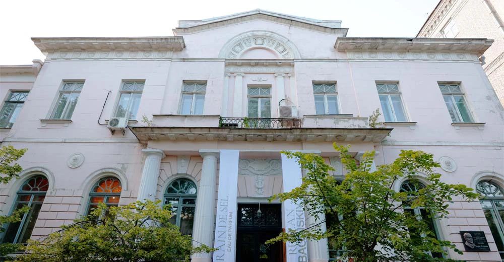 La fotografía muestra la fachada de un edificio con paredes blancas y ventanas verdes.