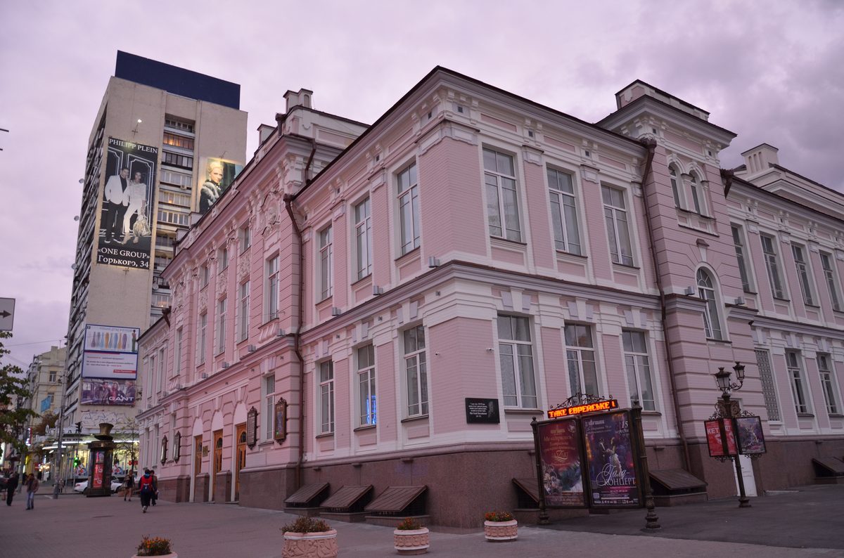 Ein Gebäude mit rosa Wänden und großen Fenstern befindet sich an einer Straße mit Werbetafeln.