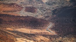 L'immagine mostra un paesaggio desertico con formazioni montuose e una strada tortuosa.