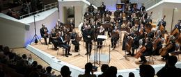 Ein Orchester spielt auf der Bühne, Musiker spielen verschiedene Instrumente.