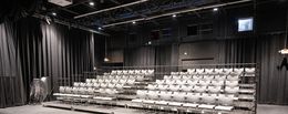 Una vista di una sala teatrale vuota con file di sedie grigie.