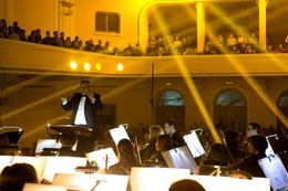 Un'orchestra si esibisce sul palco sotto la direzione di un direttore in una sala da concerto.