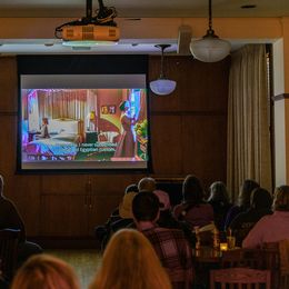 Los miembros de la audiencia están sentados en una sala viendo una película en una pantalla grande.