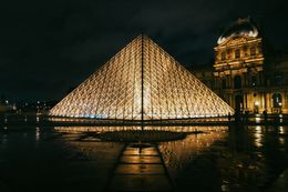 La piramide di vetro del Louvre è illuminata di notte, riflettendo il pavimento bagnato.