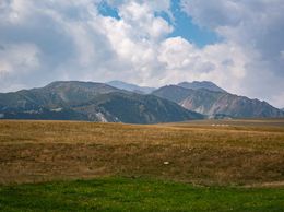 Montagne visibili all'orizzonte sotto le nuvole, con erba verde in primo piano.