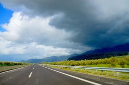Una strada chiara si estende attraverso campi verdi sotto un cielo nuvoloso.
