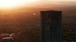 Die Stadtsilhouette ist während des Sonnenuntergangs sichtbar, mit einem hohen Gebäude im Vordergrund.