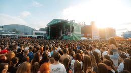 Un grande concerto si svolge sul palco, con una folla enorme radunata davanti.