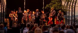 Un ensemble musicale si esibisce sul palco sotto il cielo serale.