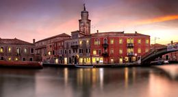 La scena presenta edifici con finestre che si affacciano su un canale al tramonto.