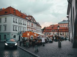 На вулиці з бруківкою розташовані кафе з терасами та старовинні будівлі.