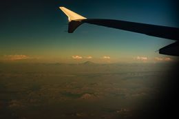 Das Bild zeigt den Flügel eines Flugzeugs, das über eine bergige Landschaft fliegt.